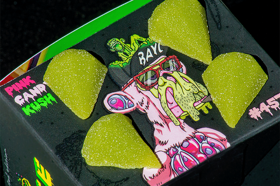 A dark green box with 'PINK CANDY KUSH' written on the cover, featuring a cartoonish face and green diamond-shaped candies