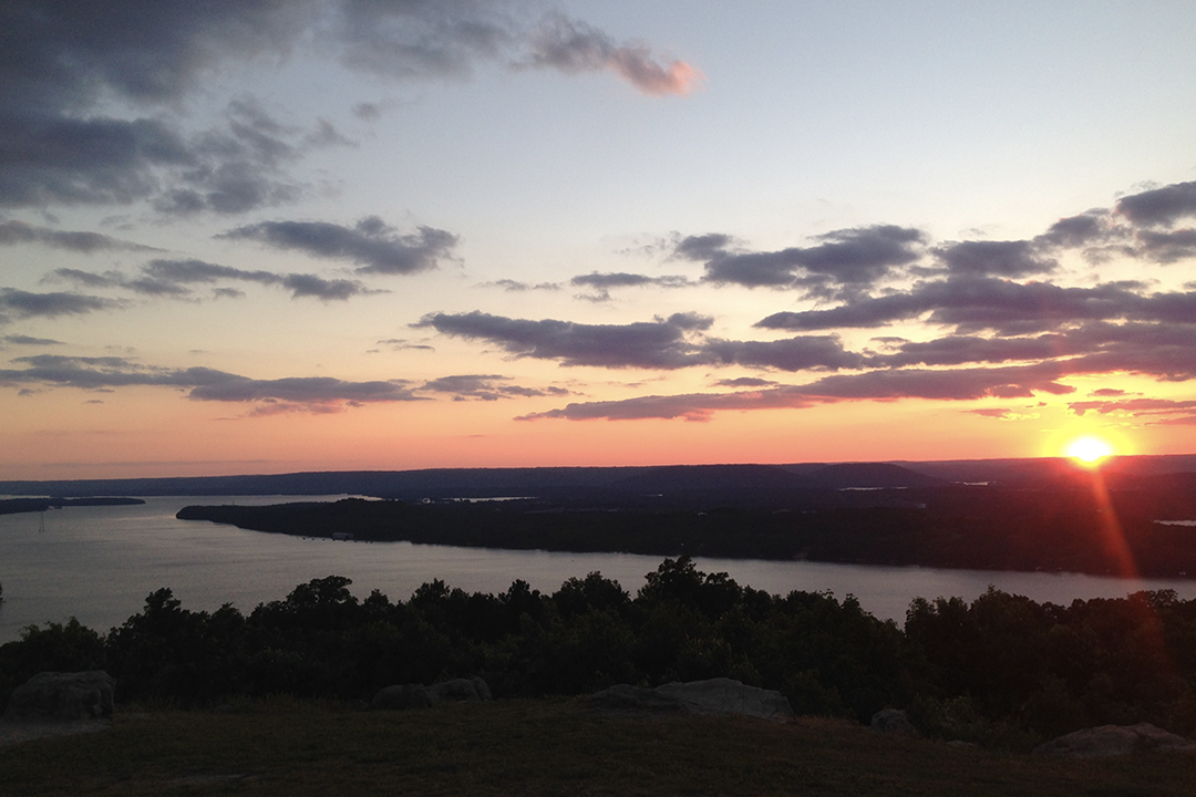 A picturesque sunset over Tennessee River in Alabama, with tree-lined banks and a serene field