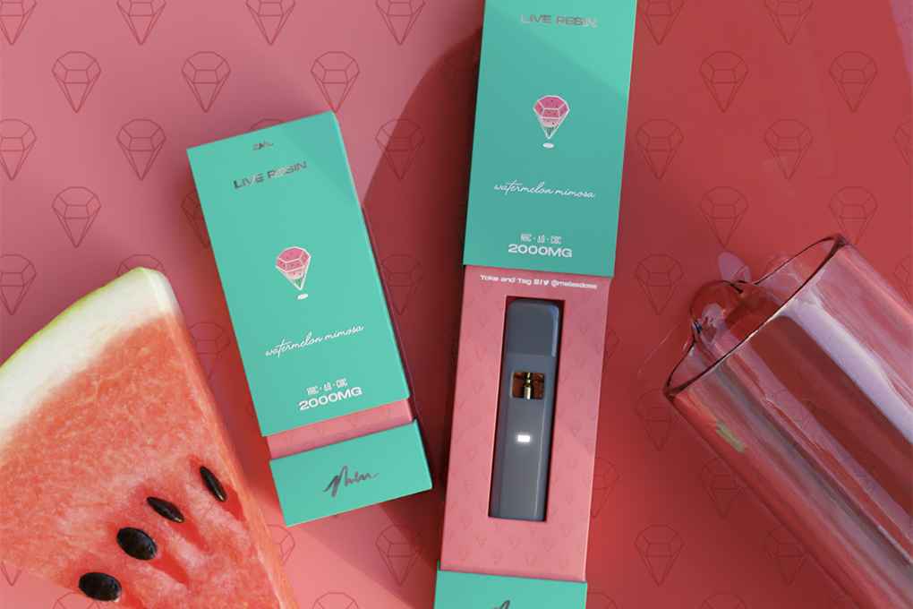 Two vibrant green 2000MG Live Resin Disposable vape packs, one of which is opened, next to the packs, there is a juicy slice of watermelon and a glass placed on a pink surface