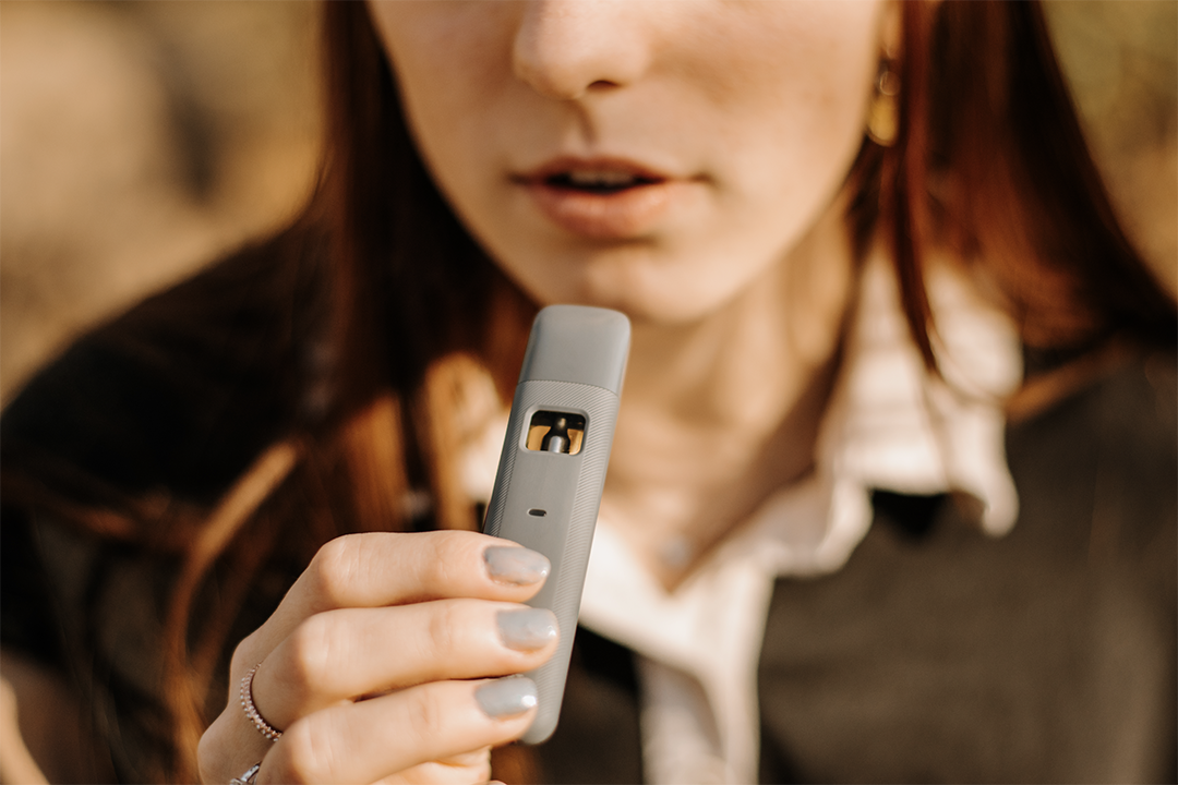 A woman delicately holds a vape cartridge in her hand, with her mouth slightly ajar in anticipation